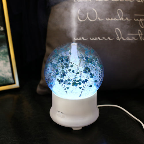 Diffuseur fleur lumineuse modèle ciel étoilé allumé en bleu sur une table de nuit, brume visible
