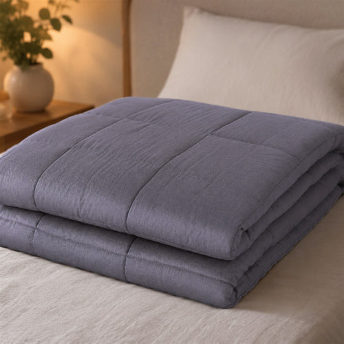 Couverture lestée Sérénuit gris ardoise, pliée sur un lit, lampe de chevet allumée